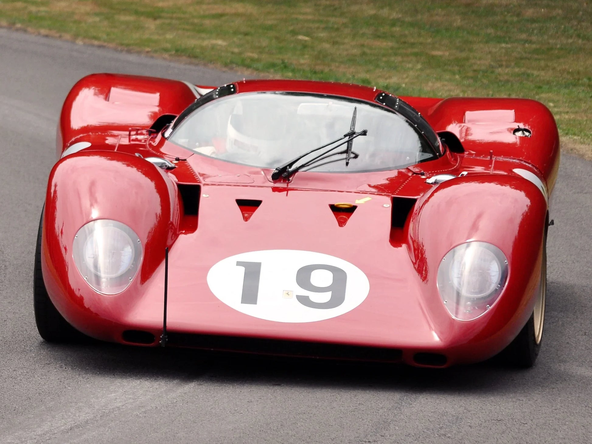 Red vintage Ferrari race car number 19 on racetrack with aerodynamic body and dual windshield wipers