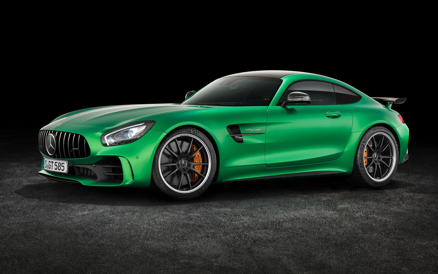 Green 2016 Mercedes AMG GT sports car with black roof and orange brake calipers on gray floor