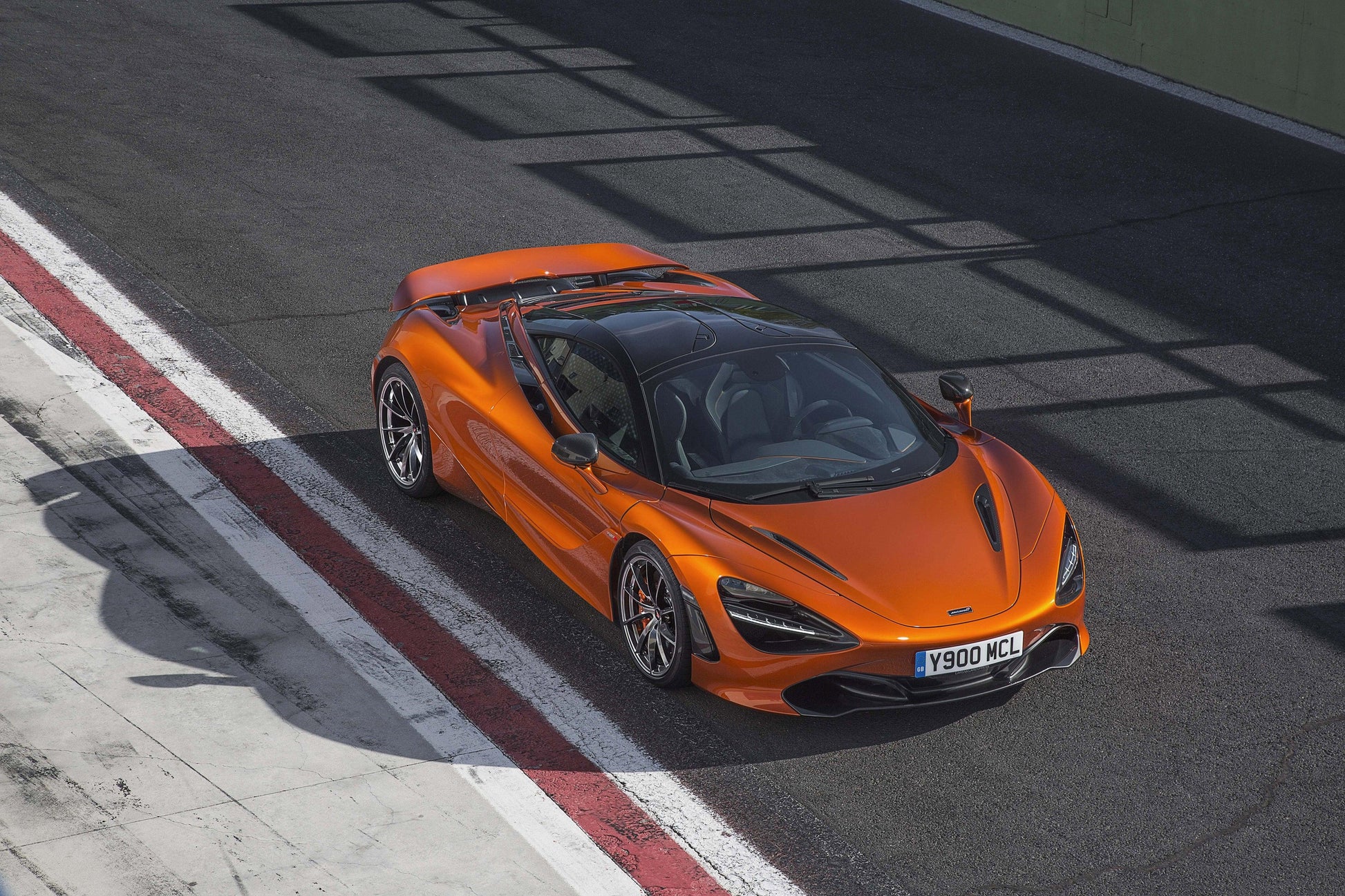 Orange McLaren 720S supercar parked on race track with black roof and sleek design