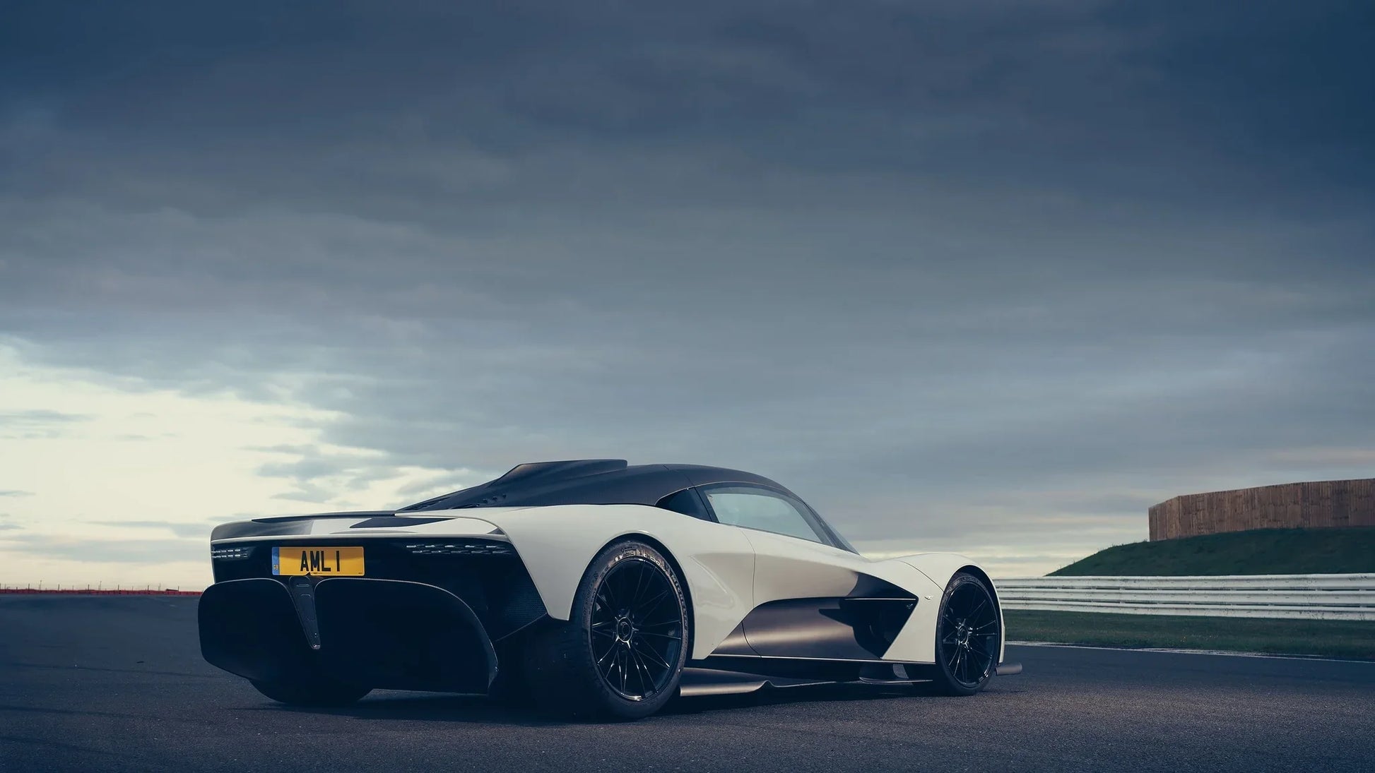 Rear view of white and black 2019 Aston Martin Valhalla sports car on race track under cloudy sky