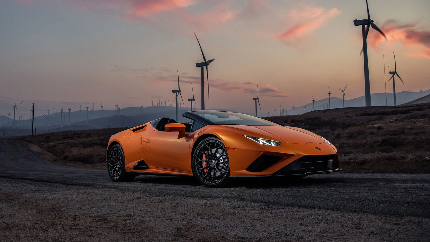 Orange Lamborghini Huracan Evo RWD Spyder parked on rural road with wind turbines at sunset
