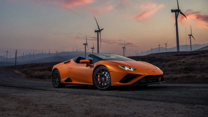 Orange Lamborghini Huracan Evo RWD Spyder parked on rural road with wind turbines at sunset