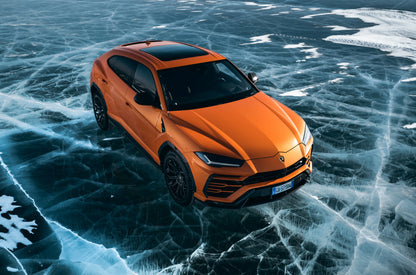 Orange Lamborghini Urus SUV on cracked frozen lake surface with black wheels