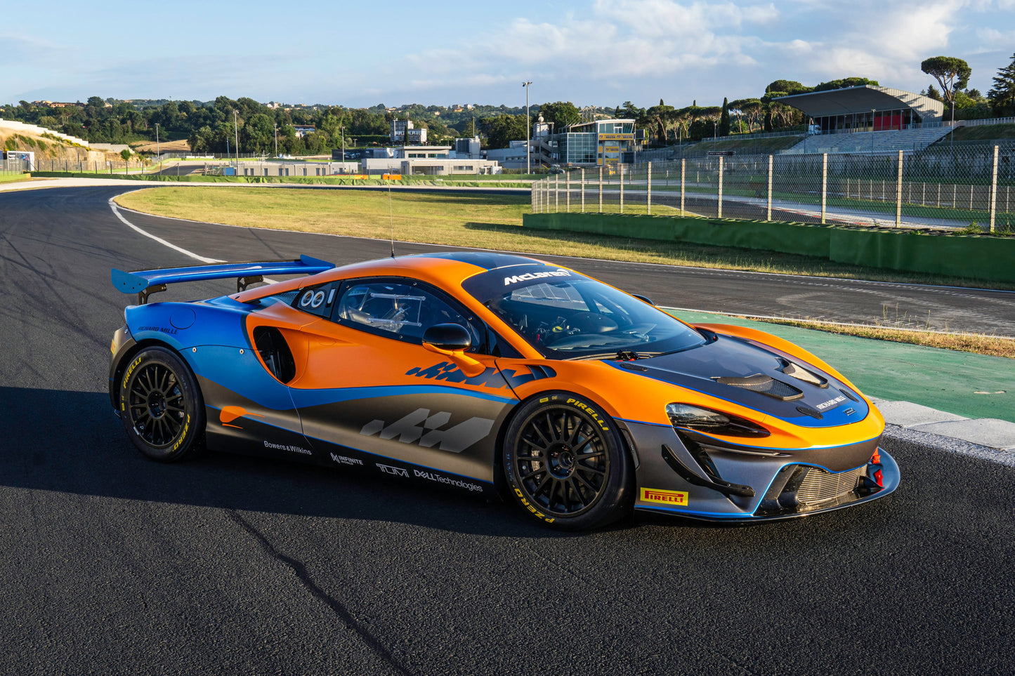 Orange and blue McLaren Artura GT4 race car on professional race track under clear sky