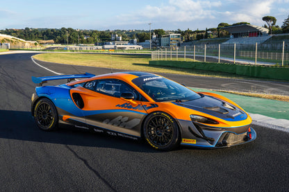 Orange and blue McLaren Artura GT4 race car on professional race track under clear sky