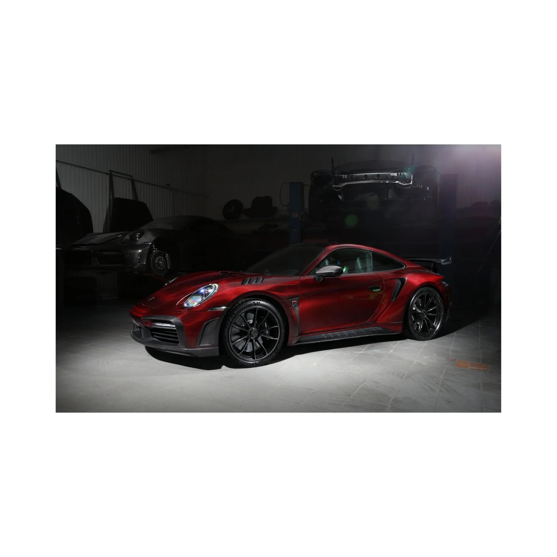 Red sports car with black rims in a dimly lit garage with other vehicles in the background