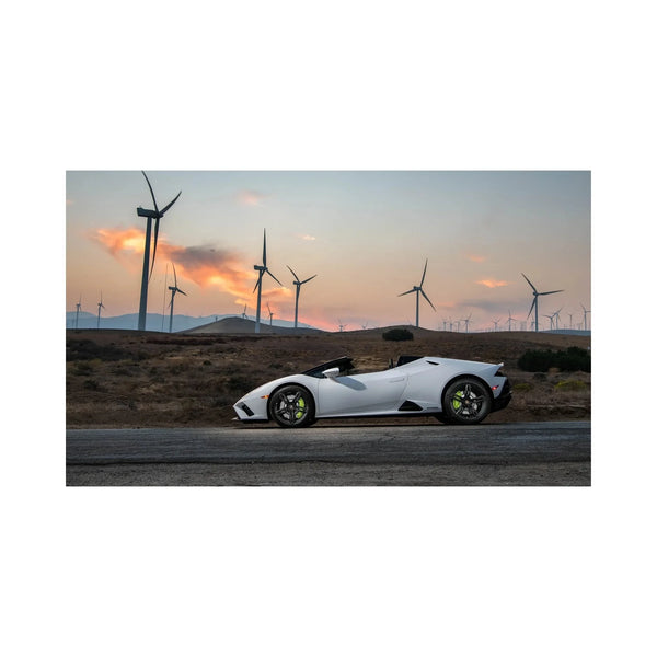 White convertible sports car parked on road at sunset with wind turbines in background
