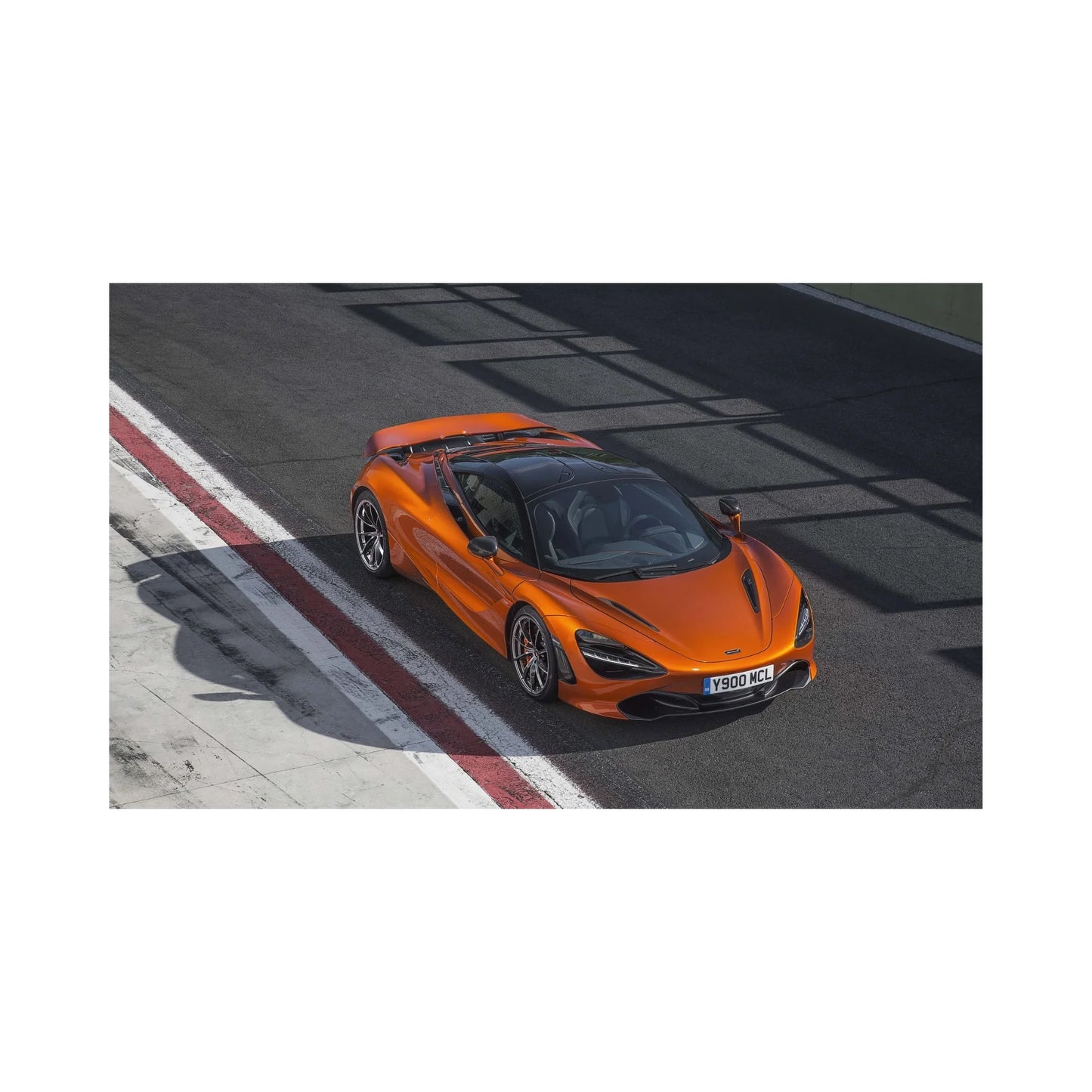 Orange McLaren sports car parked on race track next to red and white curb